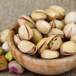 Pistachio nuts with and without shell in wooden bowl, close up